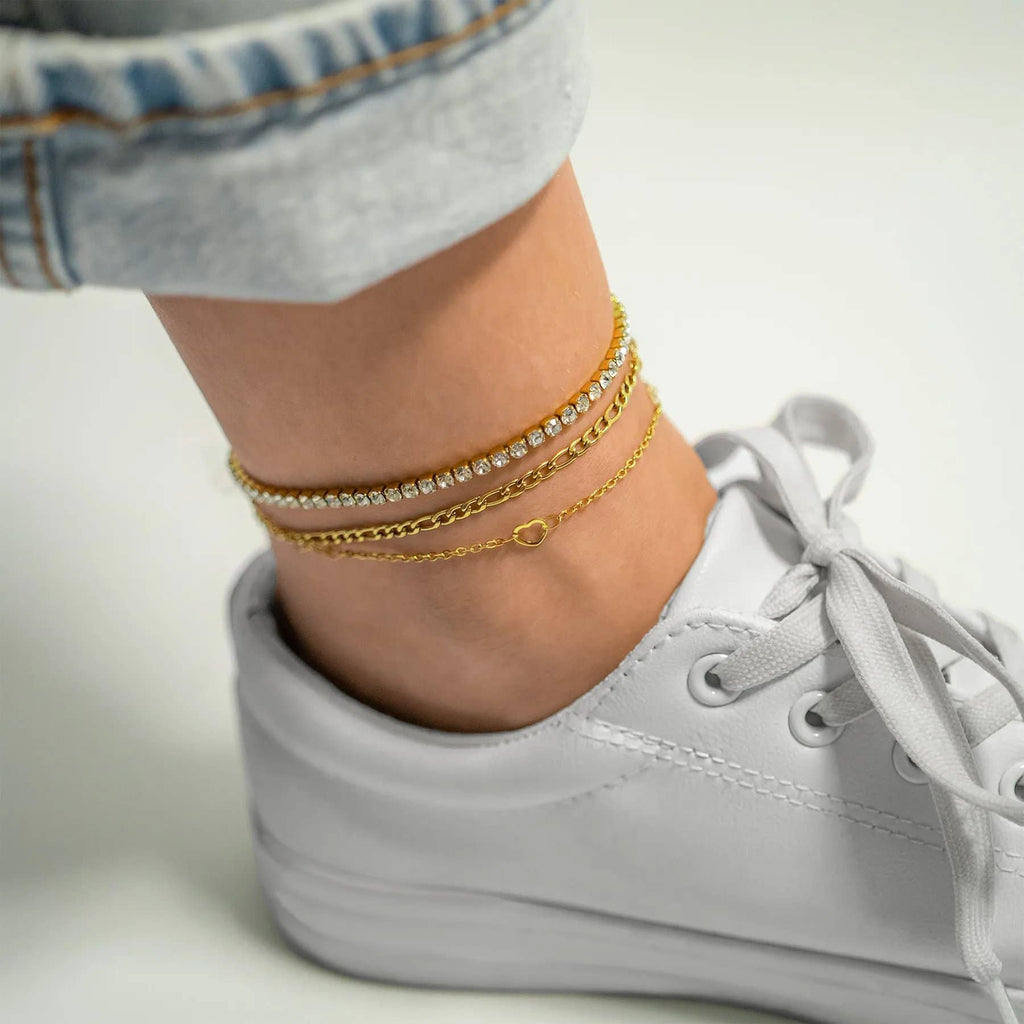 White sneakers worn with gold anklets on a neutral background