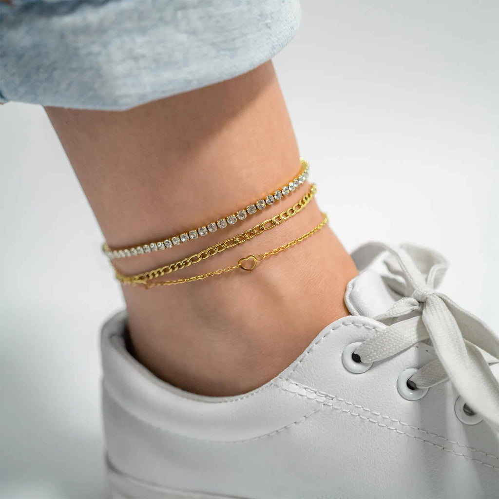 Gold anklets on a person's ankle with a white sneaker