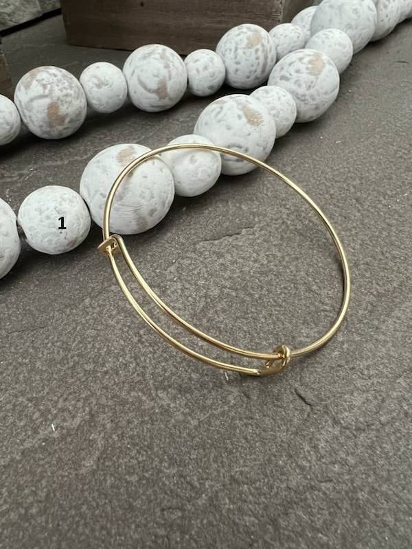 Gold bracelet on a gray surface with white spherical objects in the background