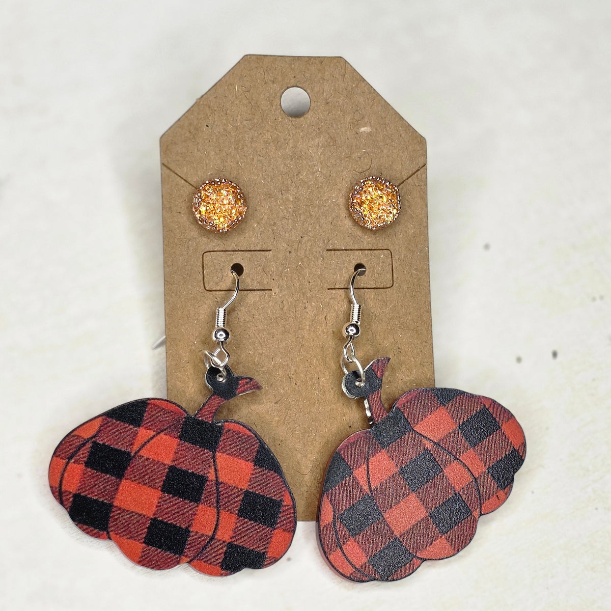 Red and black buffalo plaid pumpkin dangle earrings and sparkly golden round stud earrings on a display card