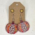 Orange and leopard-print pumpkin dangle earrings with glittery gold-tone round studs on a brown display card